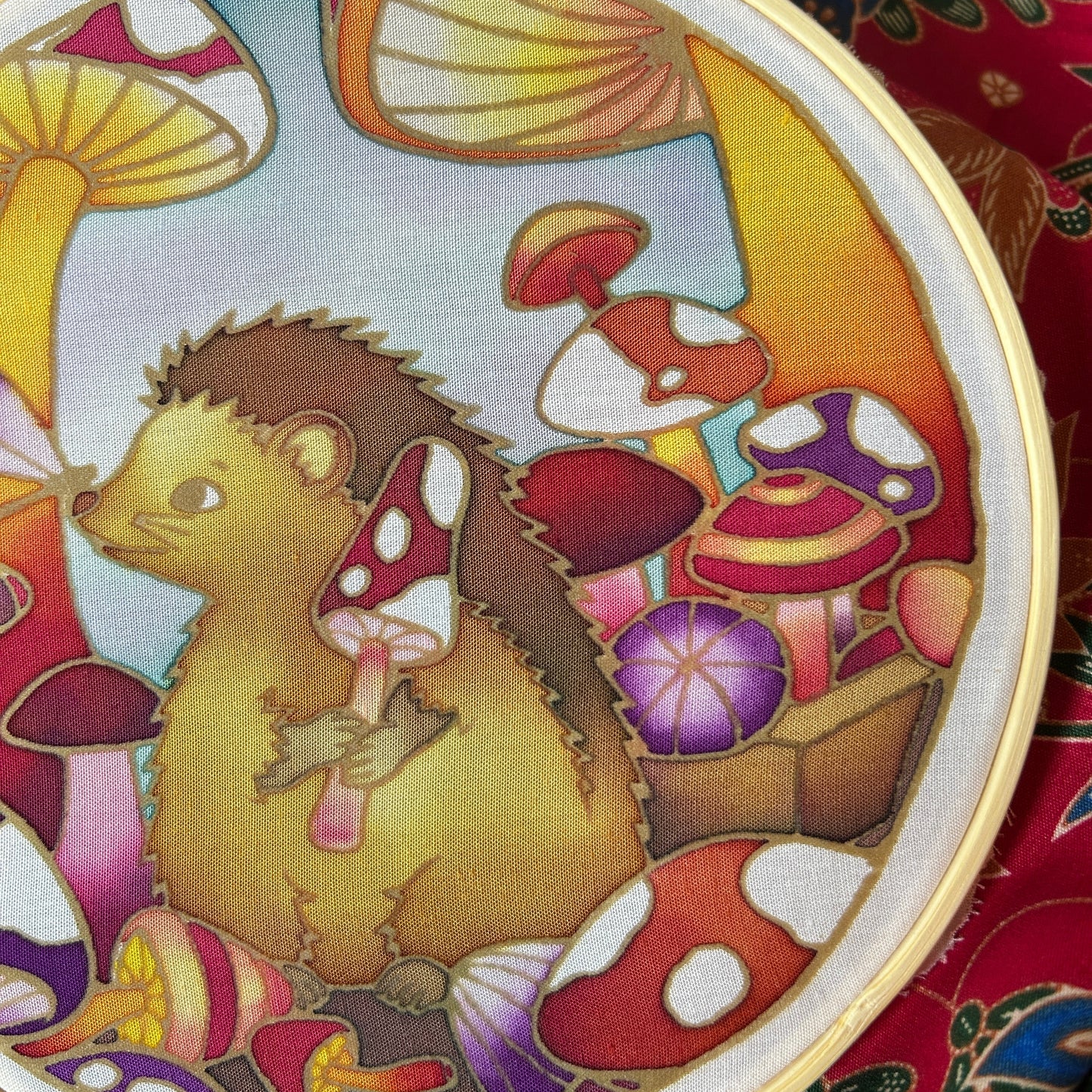 Close-up of Down the Mushroom Hole hand-painted batik artwork showing hedgehog among colourful toadstools