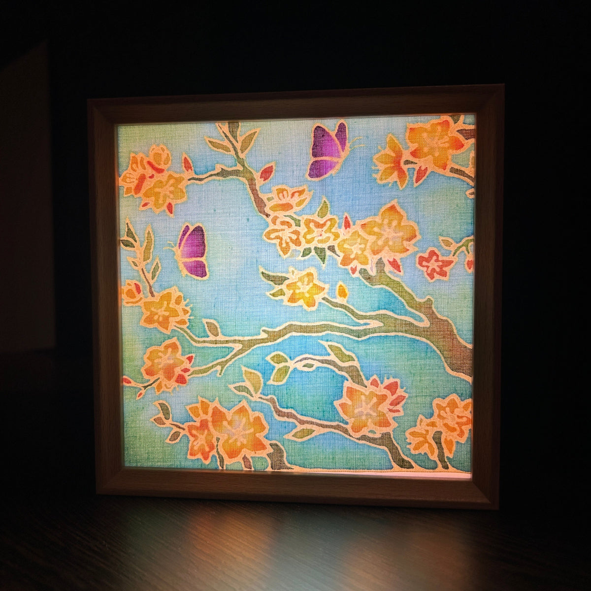 Batik Lamp Kit — Almond Blossom. Completed lamp lit from inside, showing the blossom branches and purple beetles glowing softly through the cotton. By Batik Ying.