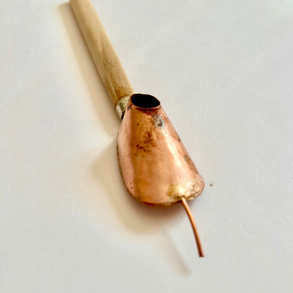 A traditional batik tjanting tool with a wooden handle and copper wax reservoir, featuring a fine spout for applying hot wax onto fabric.