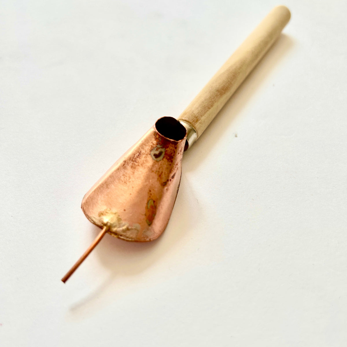 A traditional batik tjanting tool with a wooden handle and copper wax reservoir, featuring a fine spout for applying hot wax onto fabric.