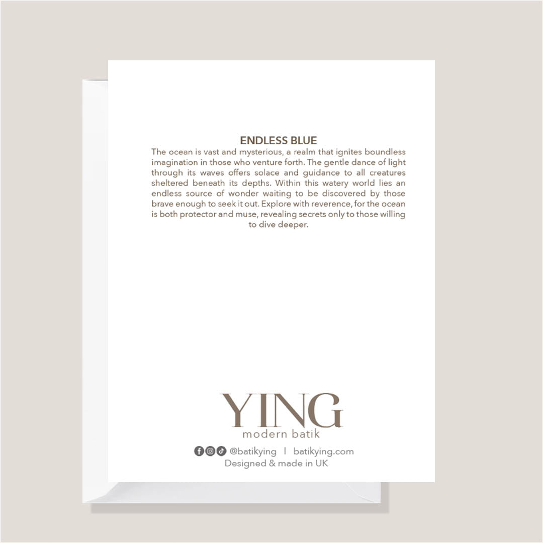 A white rectangular card or envelope with printed text, shown standing upright on a light gray surface against a warm beige background. The visible text includes the title 'ENDLESS BLUE' and branding at the bottom reading 'YING modern batik' with social details and 'Designed & made in UK'.